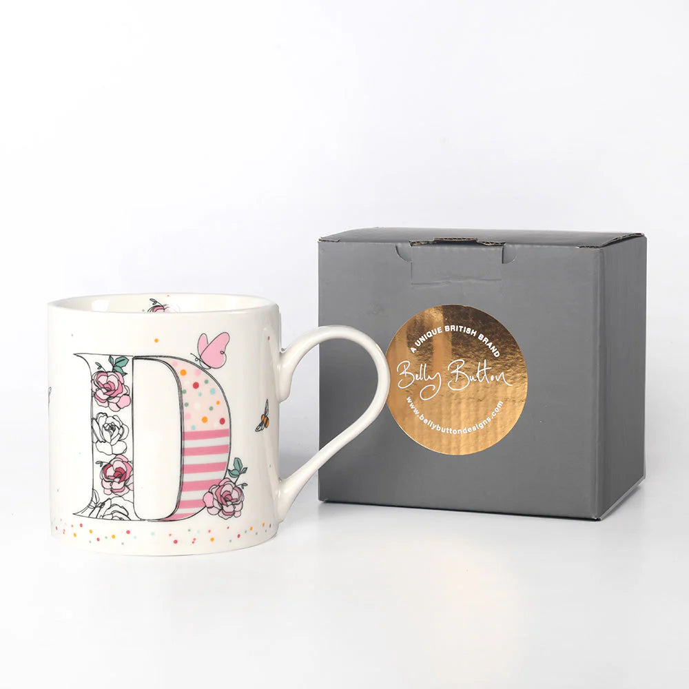 A white ceramic mug with a colorful floral and animal pattern, featuring the letter 'D' in the center, presented next to a gray presentation box with a gold foil stamp.