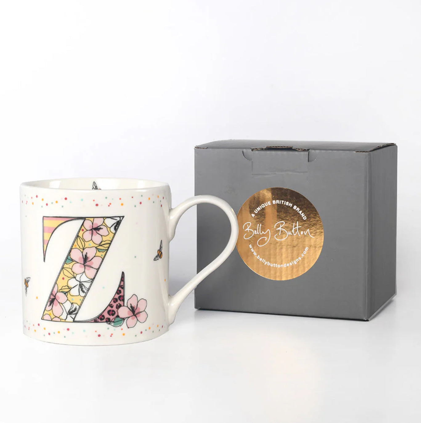 A white ceramic mug with a colorful floral pattern and the monogram 'Z' on the front, displayed next to a gray presentation box with a foil stamp on the lid.