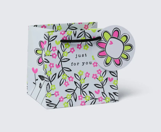 A multicolored gift bag with a floral pattern, featuring a woven paper handle and a gift tag.