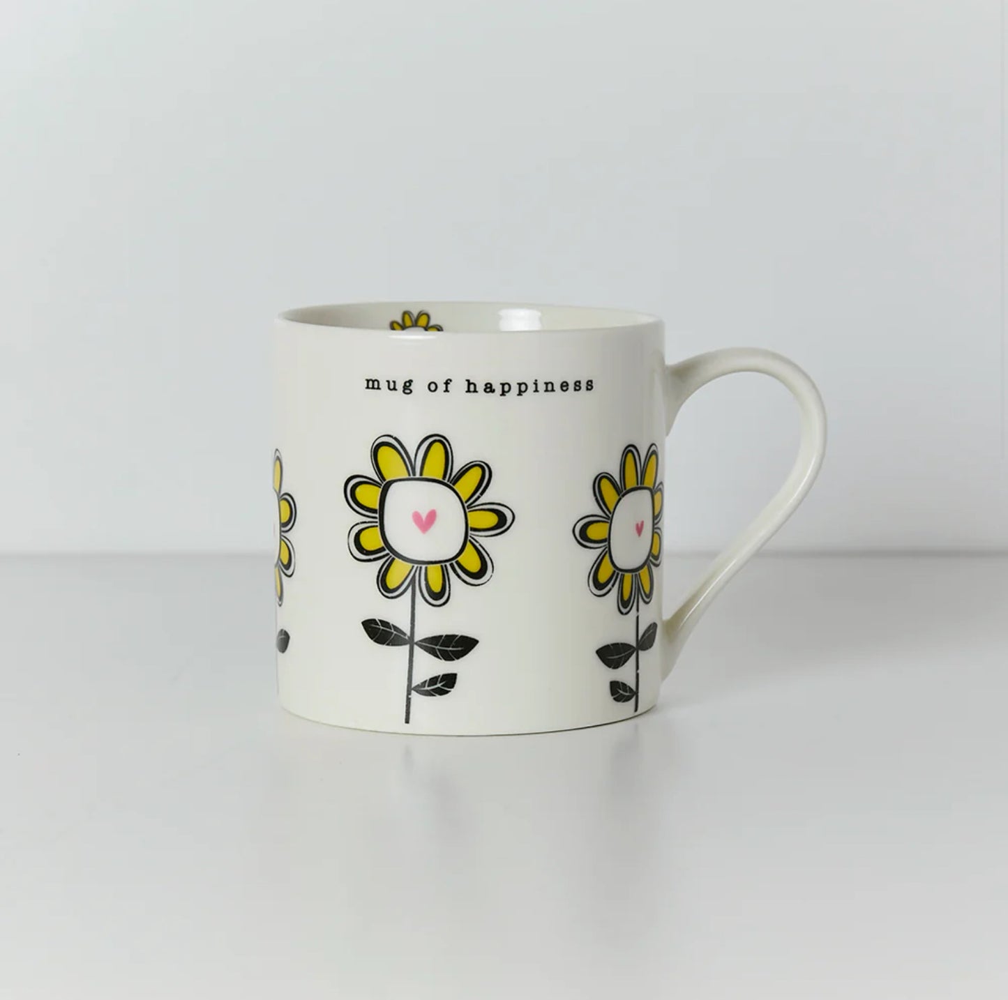 A white ceramic mug with a yellow and black floral pattern and the text 'Mug of Happiness' on it.