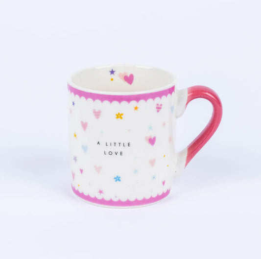 A white china mug with pink accents and multicolored design, featuring the text 'A LITTLE LOVE' and various shapes like hearts and stars.