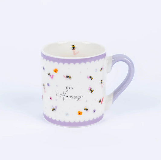 A small white china mug with a purple rim and handle, featuring a bee design and the text 'BE HAPPY' on the front.