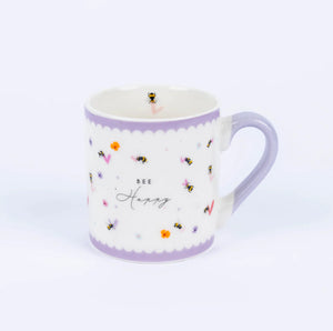 A small white china mug with a purple rim and handle, featuring a bee design and the text 'BE HAPPY' on the front.