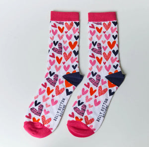 A pair of socks with a pattern of big hearts in various colors on a white background, with pink cuffs.
