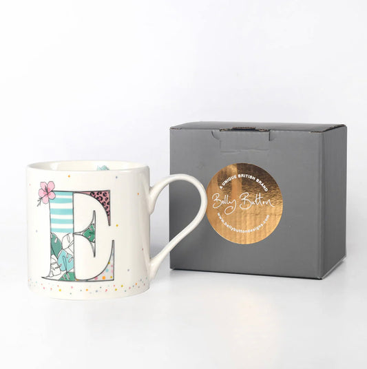 A white ceramic mug with a multicolor floral and animal pattern and a large gold letter 'E' in the center. The mug is displayed next to a gray presentation box with a foil stamp on the lid.