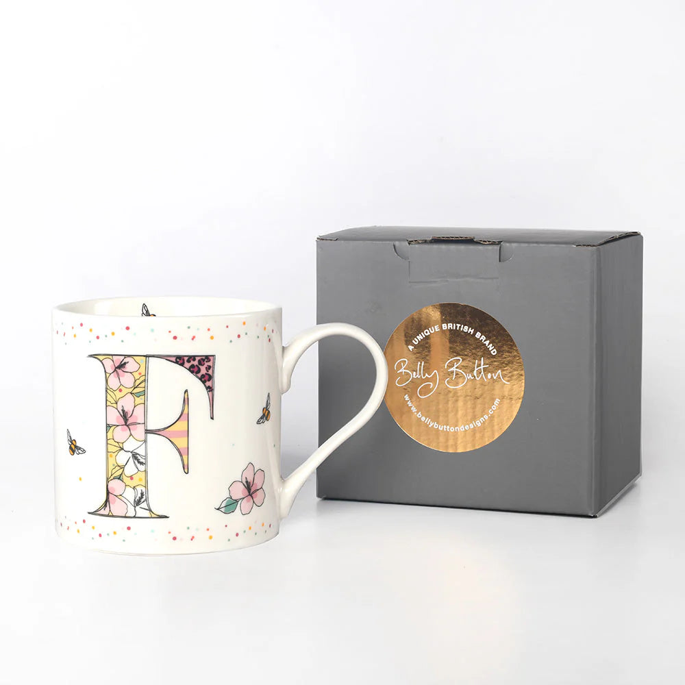 A white china mug with a colorful floral and insect design, featuring the monogram initial 'F', and a grey presentation box with 'Belly Button Designs' branded on it.