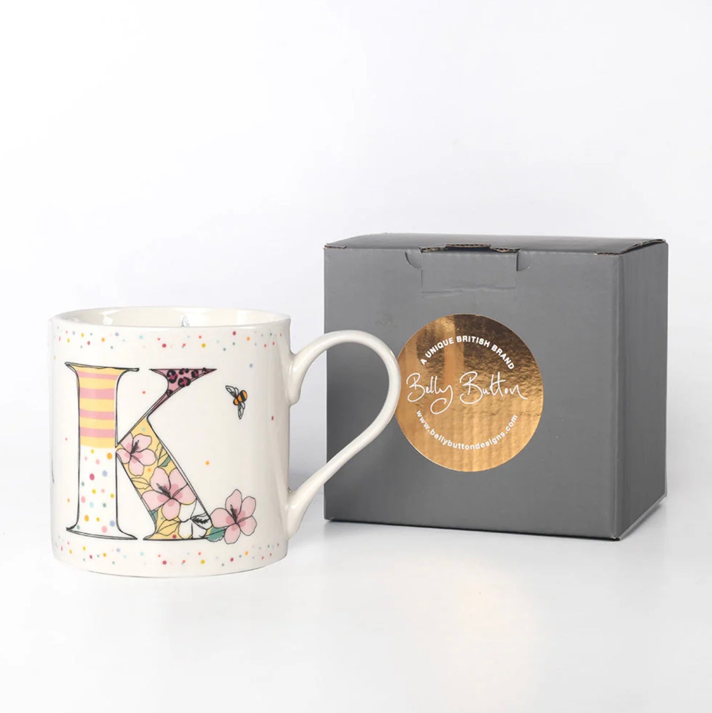 A white ceramic mug with a colorful floral and insect pattern, featuring the monogram initial 'K'. The mug is presented alongside a gray presentation box with a foil stamp on the lid.