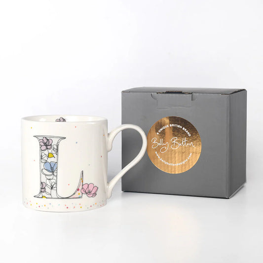 A white ceramic mug with a colorful floral and animal pattern, featuring a monogram initial 'L' on the front. The mug is displayed next to a gray presentation box with a foil stamp on the lid.