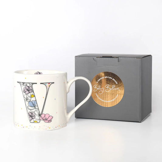 A white ceramic mug with a colorful floral pattern and the monogram initial 'V' on it, accompanied by a grey presentation box with a foil stamp on the lid.