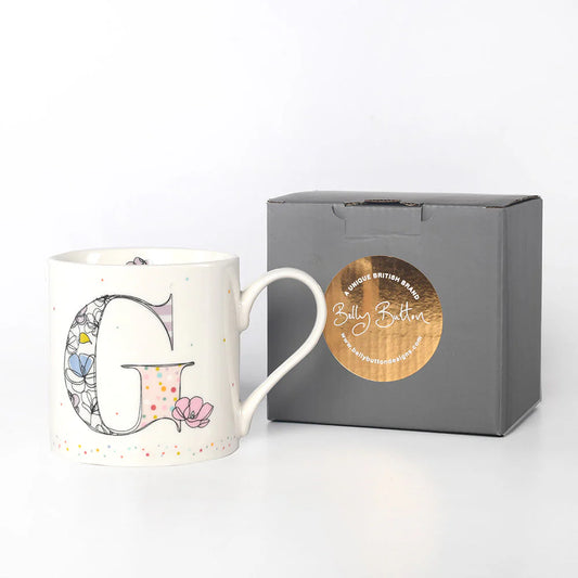 A white china mug with a colorful floral pattern and the monogram initial 'G' on the front, accompanied by a grey presentation box with a foil stamp on the top.