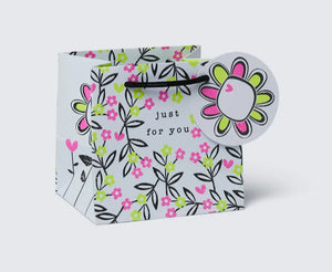 A multicolored gift bag with a floral pattern, featuring a woven paper handle and a gift tag.