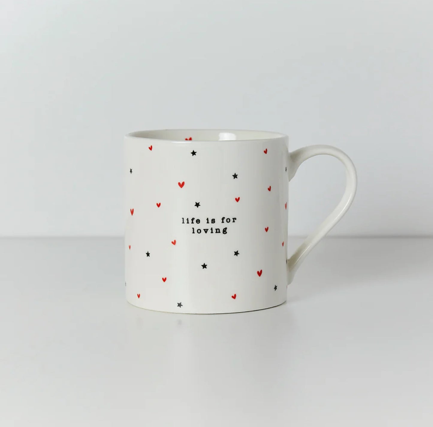 A white ceramic mug with a red and black heart pattern and the text 'life is for loving' on it.
