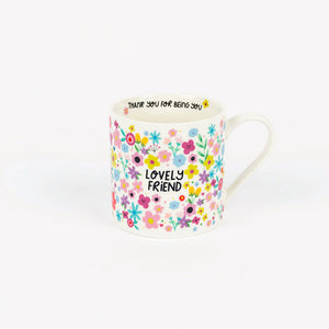 White ceramic mug with colorful floral pattern and the words “Lovely Friend” on the front, and the phrase “Thank you for being you” printed inside the rim.
