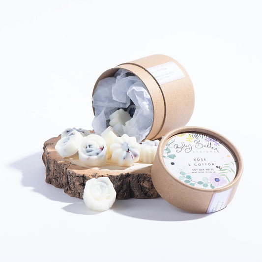 A collection of flower-shaped scented soy wax melts displayed next to an open cylindrical cardboard packaging with a label.