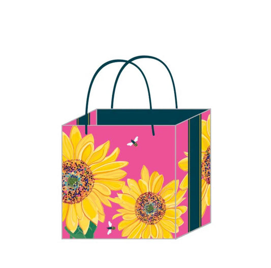 A rectangular gift bag with a pink background featuring a large sunflower design, woven paper handle, and a black gift tag.