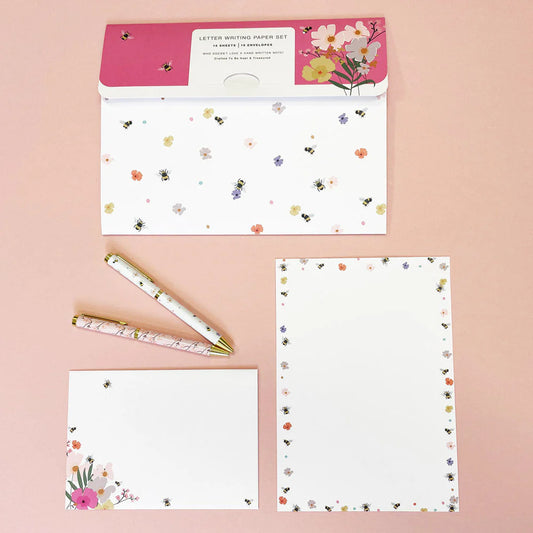 A writing set including 15 A5 sheets with floral and insect patterns, 10 envelopes, and a coordinating reusable wallet, all displayed on a pink background.