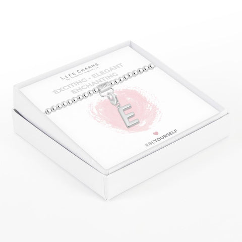 Initial charm bracelet with the letter E, presented on a silver foiled card with the text 'EXCITING • ELEGANT • ENCHANTING' and the brand name 'LIFE CHARMS'. The bracelet is silver, and the card has a pink background with a heart shape.