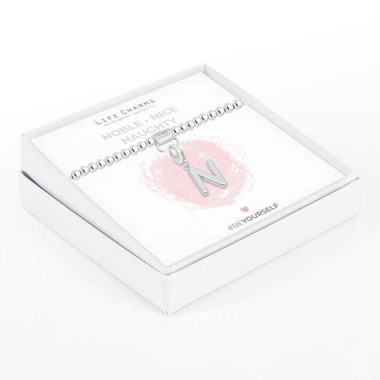 Initial charm bracelet with the letter N, presented on a silver foiled card with the text 'NOBLE • NICE • NAUGHTY' and the brand name 'LIFE CHARMS'. The bracelet is silver, and the card has a pink background with a heart shape.